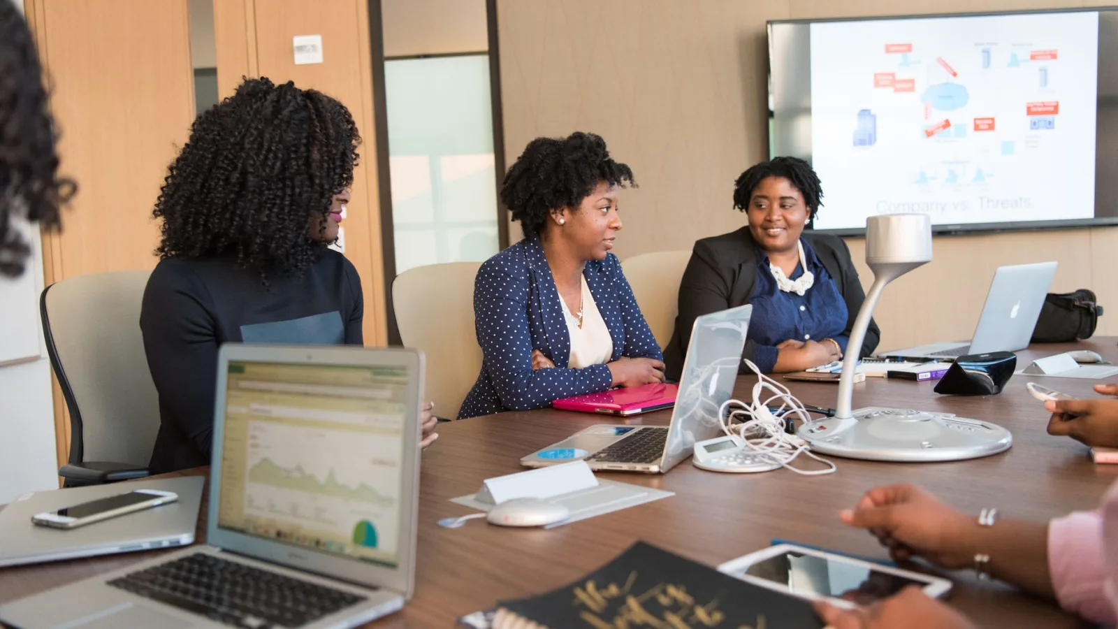 Four diverse women engaged in a business meeting with laptops and presentations in an office.