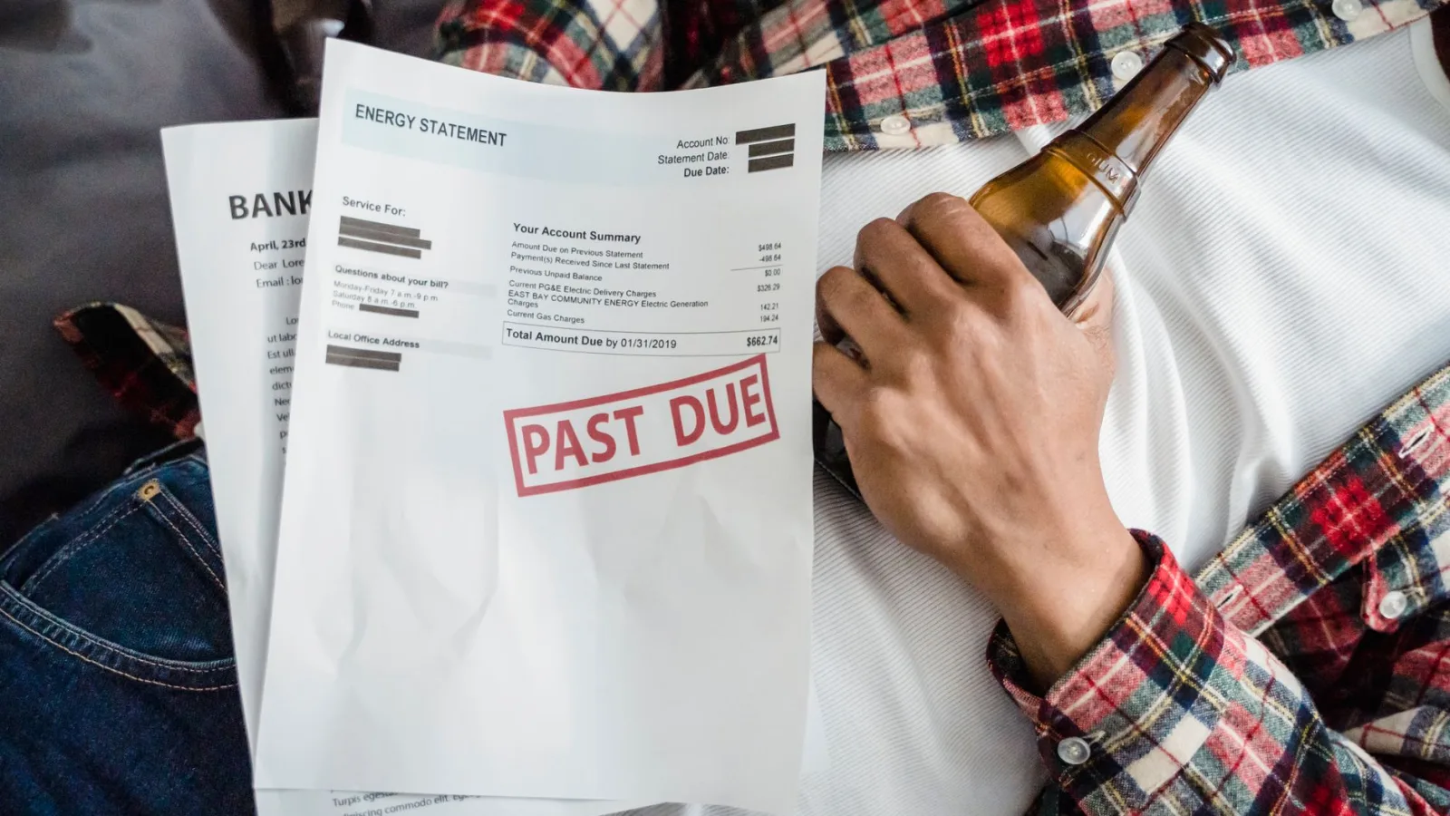 A man relaxes with a beer bottle while holding past due bills, highlighting financial stress.