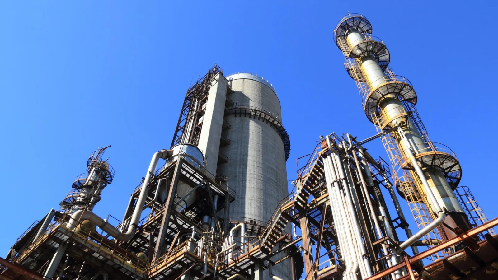A towering industrial plant under a vivid blue sky, showcasing its intricate architecture and industrial prowess.