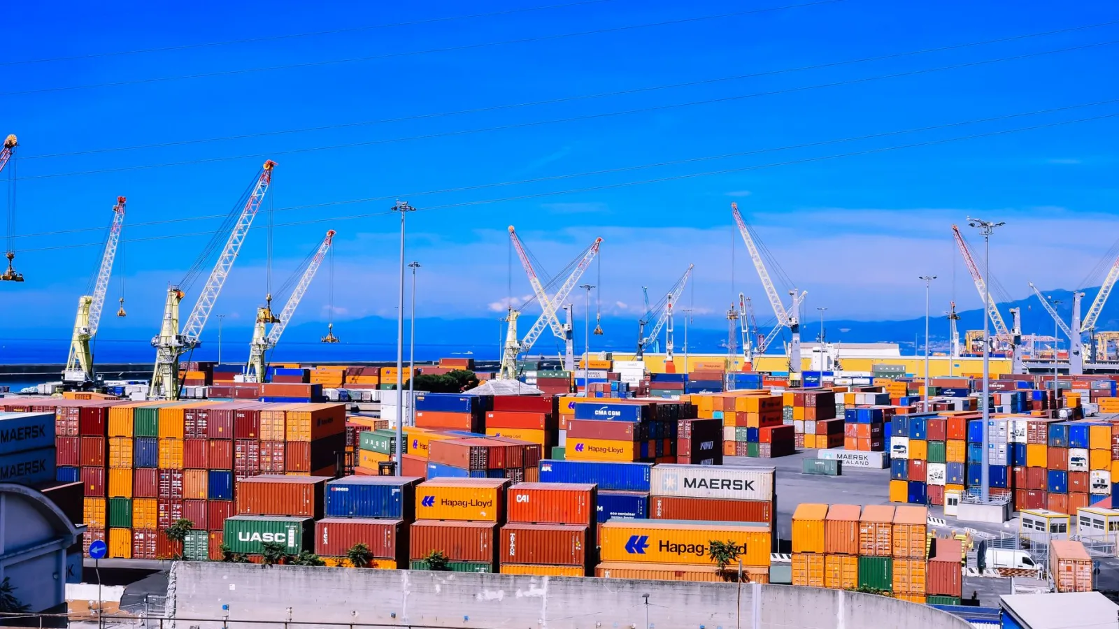 A bustling shipping port with colorful stacked containers and numerous cranes under a clear blue sky.