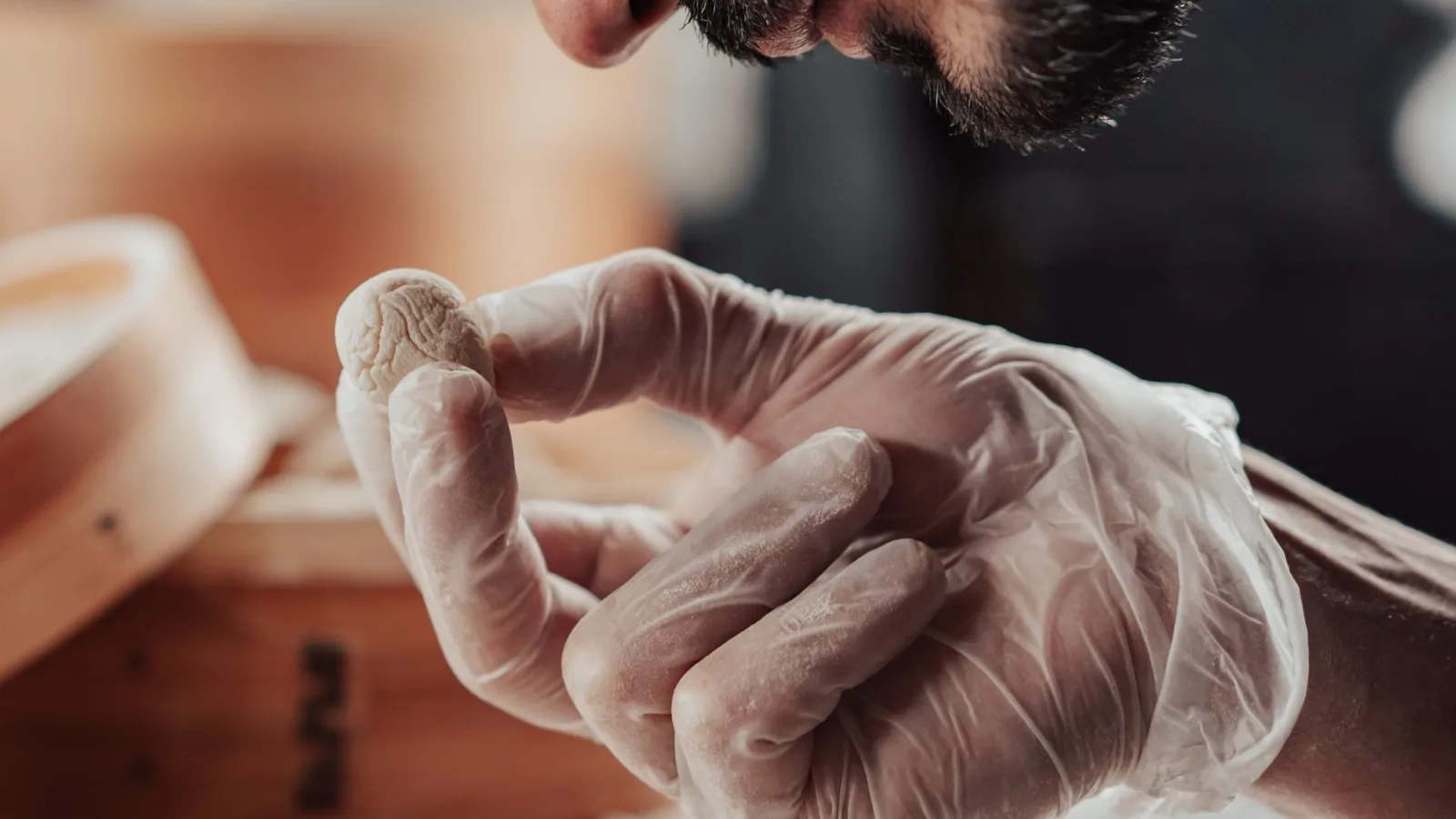 Person wearing gloves closely examining a small dough piece, focusing on details.